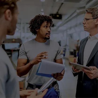3 personnes en train de discuter dans une pièce avec des papiers et tablettes à la main