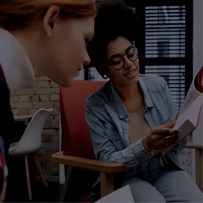 Deux femmes qui regardent un livre. L'une d'elle montre une info