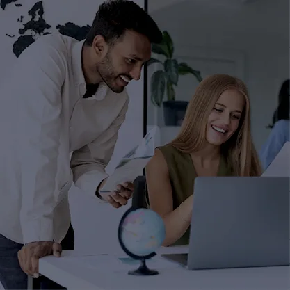 Deux personnes souriantes en train de travailler sur ordinateur avec un globe sur le bureau 