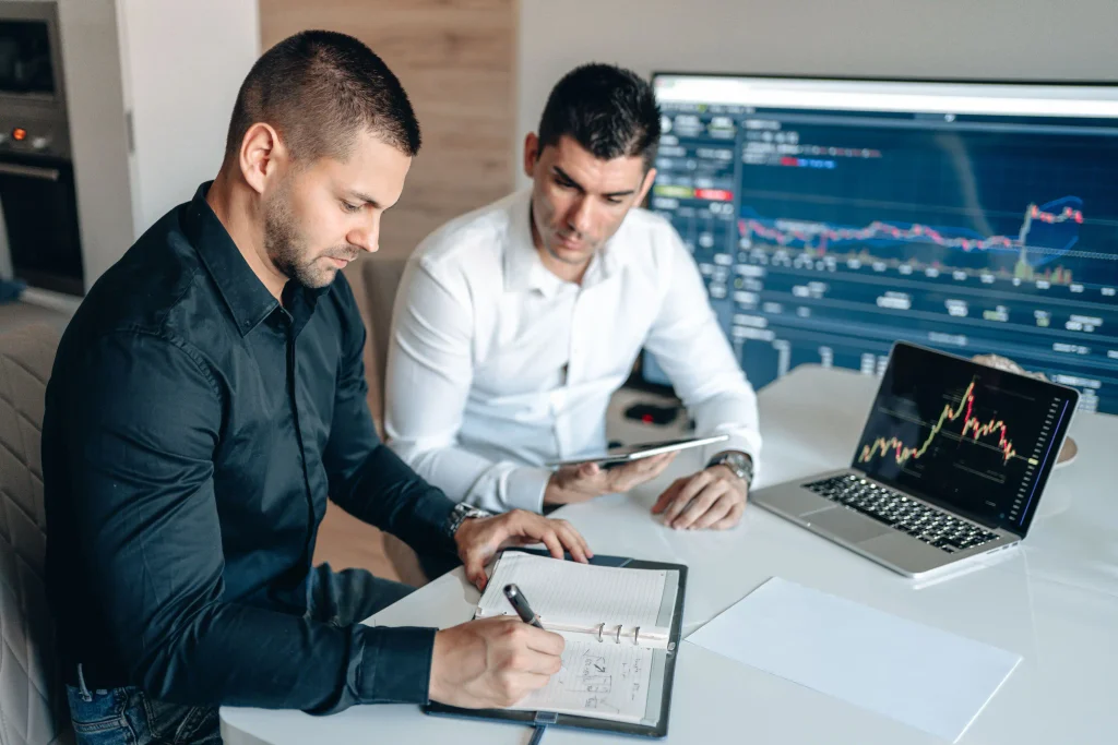 Deux commerciaux analysant des données financières avec des appareils numériques et des graphiques dans un cadre de bureau